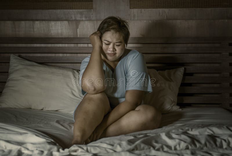 Dramatic portrait of young sad and depressed fat and chubby Asian girl crying helpless on bed at home victim of bullying and