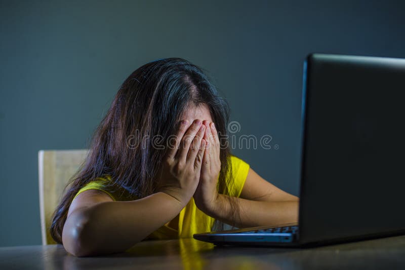 Dramatic portrait of young sad and scared woman covering face with hands stressed and worried looking at laptop computer isolated