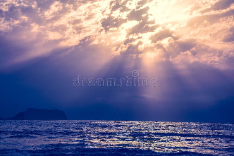 Seascape with sun rays piercing through clouds over a serene ocean at dusk stock image