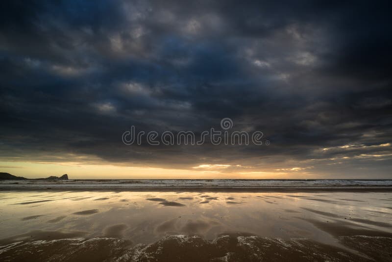 Dramatický búrlivé sky krajiny odráža v odlive voda na pláži Rhosilli Bay.