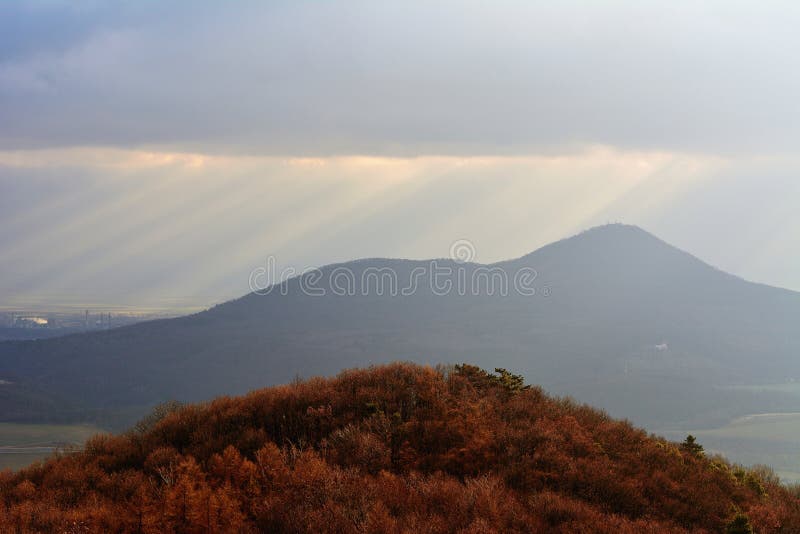 Dramatic Sun Rays Piercing Through Clouds Over Rolling Hills in Morning stock photos