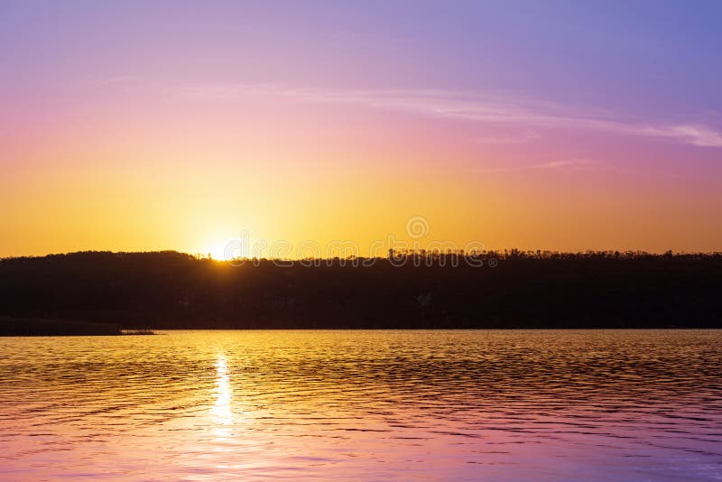 Dramatic sunset over river with orange and purple colors.Sun goes down over pond and forest silhouette. Beautiful nature backgroun