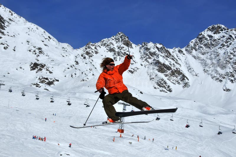 A skier showing a dramatic posture during a high jump with mountains and ski lifts in the background. A skier showing a dramatic posture during a high jump with mountains and ski lifts in the background