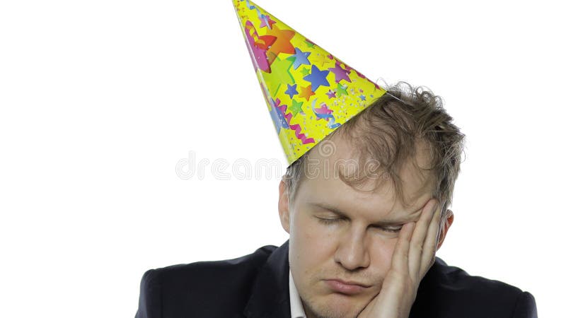 Portrait of drank sleepy young clerk man with a hangover falling asleep. Emotions. Disheveled guy businessman in suit and festive cap. White background. Office birthday party. Portrait of drank sleepy young clerk man with a hangover falling asleep. Emotions. Disheveled guy businessman in suit and festive cap. White background. Office birthday party