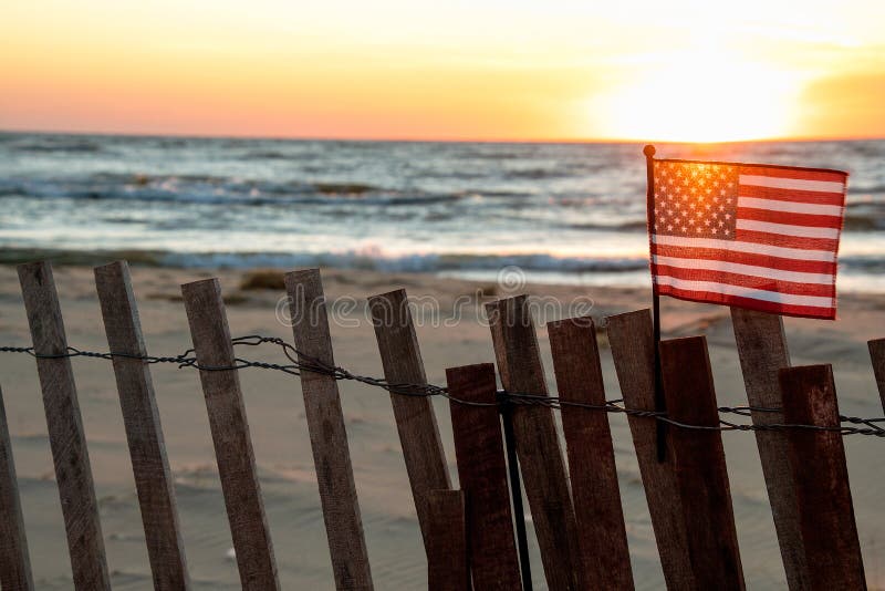 Drapeau américain sur la barrière de plage avec la lueur de coucher du soleil image libre de droits Drapeau américain sur la barrière de plage avec la lueur de coucher du soleil image libre de droits