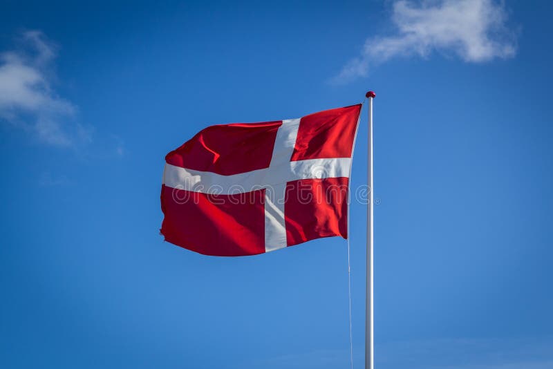 Drapeau danois en soleil contre le ciel bleu avec des nuages, horizontaux photos stock Drapeau danois en soleil contre le ciel bleu avec des nuages, horizontaux photos stock