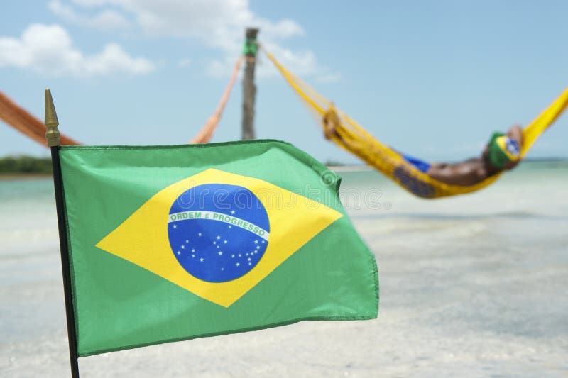Drapelul brazilian fluturând în fața hamacului de plajă. Drapelul brazilian fluturând în fața unui bărbat relaxându-se într-un hamac de plajă înșirat deasupra mării