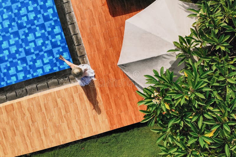 Draufsicht der jungen unerkennbaren Frau im weißen Kleid und im Strohhut, die nahe Swimmingpool sitzt ohne Gesicht drohne lizenzfreies stockfoto Draufsicht der jungen unerkennbaren Frau im weißen Kleid und im Strohhut, die nahe Swimmingpool sitzt ohne Gesicht drohne lizenzfreies stockfoto