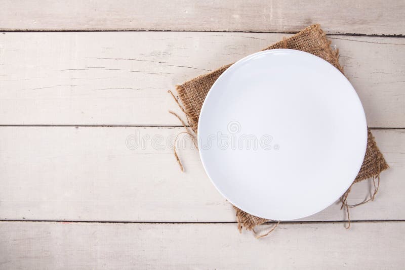 Draufsicht der leeren weißen Platte setzte an Sack und weiße hölzerne Tabelle lizenzfreies stockbild Draufsicht der leeren weißen Platte setzte an Sack und weiße hölzerne Tabelle lizenzfreies stockbild