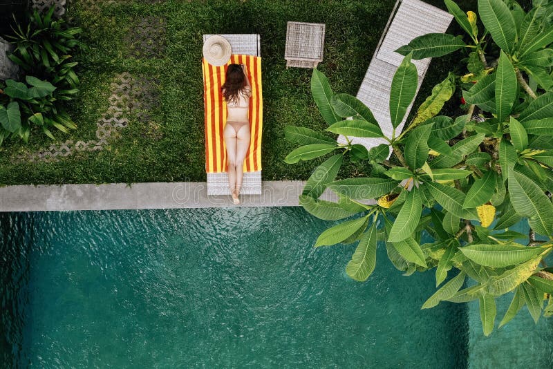 Draufsicht der unerkennbaren dünnen jungen Frau im beige entspannenden Bikini und nahe Luxusswimmingpool im Grün ein Sonnenbad ne lizenzfreie stockbilder Draufsicht der unerkennbaren dünnen jungen Frau im beige entspannenden Bikini und nahe Luxusswimmingpool im Grün ein Sonnenbad ne lizenzfreie stockbilder