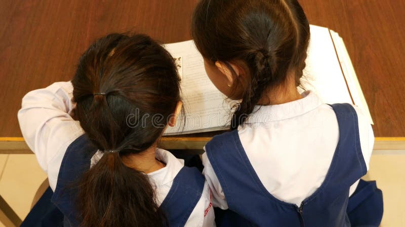 Draufsicht von kleinen asiatischen Studenten mit Uniformlesebuch in der Bibliothek zusammen