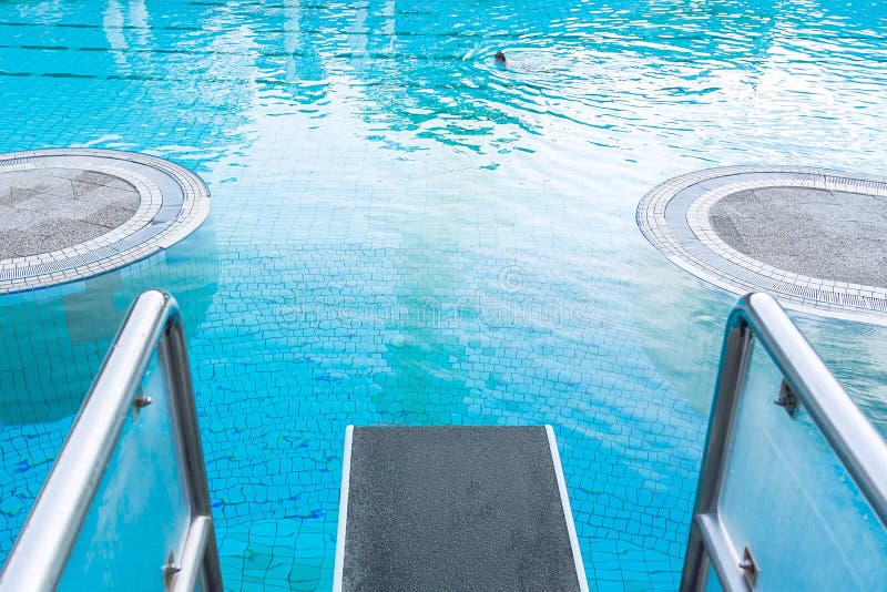 Draufsichtnahaufnahme auf einem Sprungbrett vor dem Hintergrund eines Pools mit blauem Wasser, in dem eine Person Schwimmen Das K