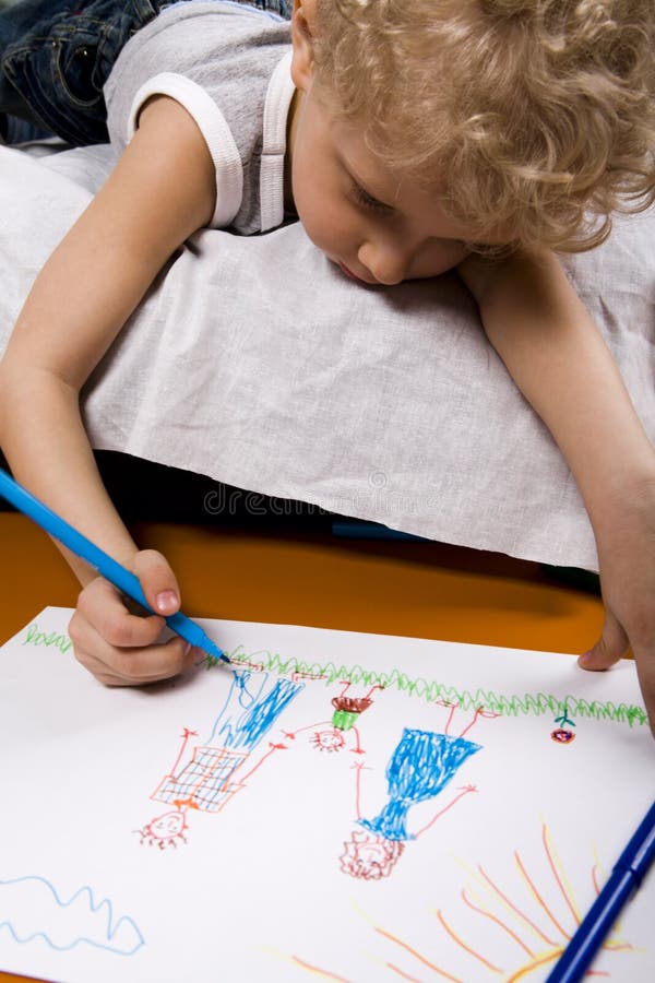 Curly blond boy lying on the bed drawing the picture of his family. Curly blond boy lying on the bed drawing the picture of his family