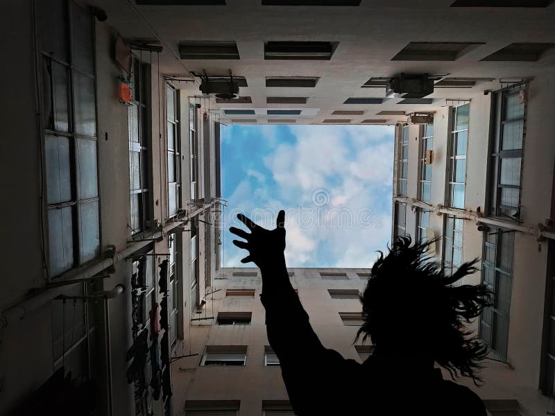 Silhouette di una persona in fondo di un edificio, alla ricerca e alzando una mano verso il cielo sopra di lei.