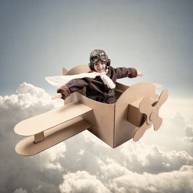 Boy wearing old-fashioned aviator hat, scarf and goggles flying a cardboard airplane in his imagination. Boy wearing old-fashioned aviator hat, scarf and goggles flying a cardboard airplane in his imagination