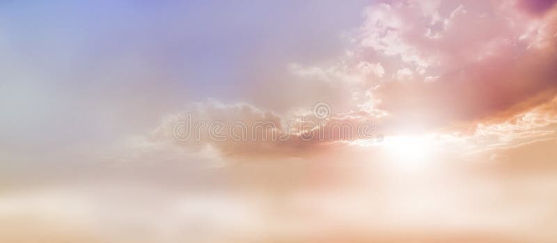 Beautiful wide peach and dusky pale blue sky and cloud scape with a burst of sunlight emerging from under the cloud base with plenty of copy space. Beautiful wide peach and dusky pale blue sky and cloud scape with a burst of sunlight emerging from under the cloud base with plenty of copy space