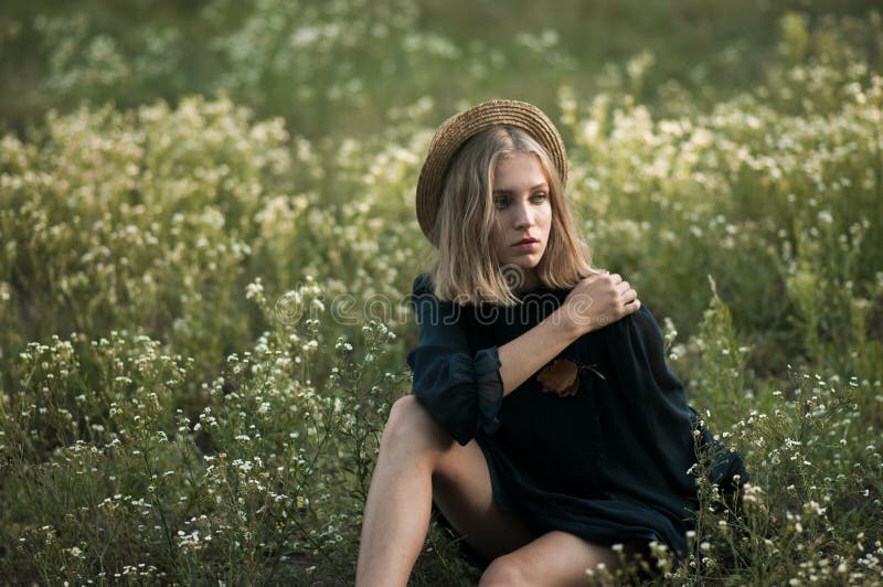 Dreamy young girl in a straw hat and black dress sitting in a f