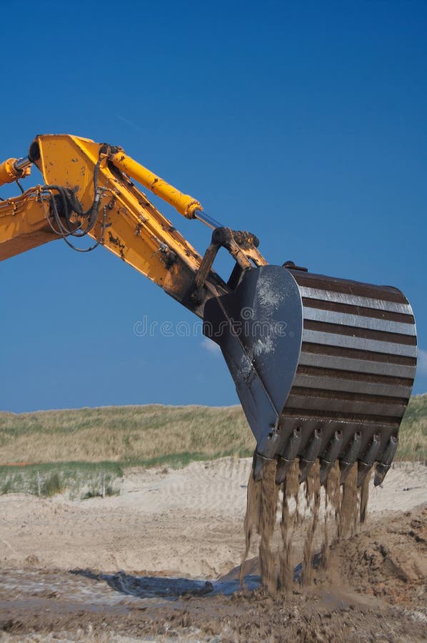 Action shot of falling sand from the steel teeth/mouth of an earth moving machine/digger. In sand with blue sky. side view. Action shot of falling sand from the steel teeth/mouth of an earth moving machine/digger. In sand with blue sky. side view.