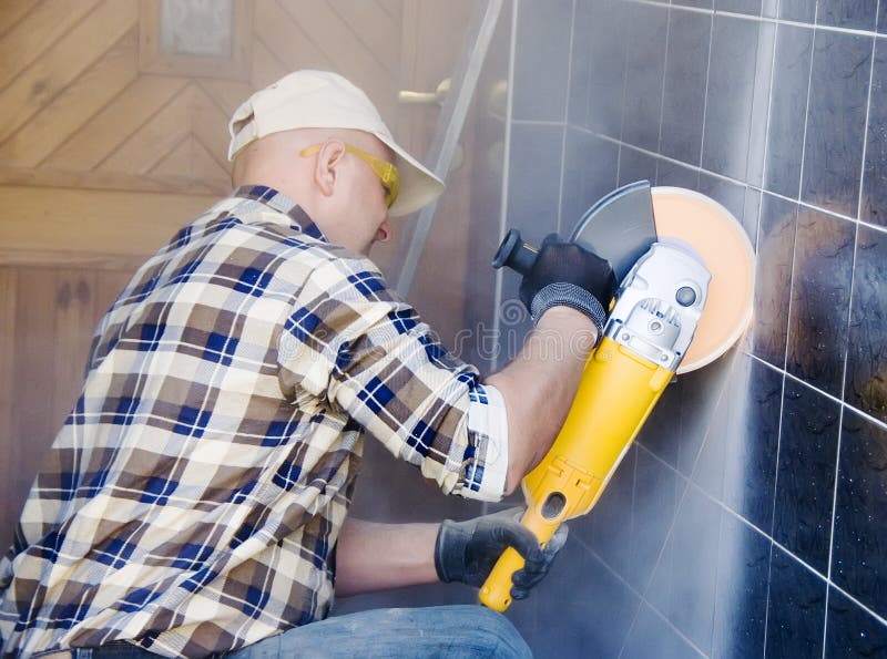 A worker drilling through some wall tiles using a mechanical rotary drill or saw, wearing protective gloves. Home renovation and remodelling abstract concept. A worker drilling through some wall tiles using a mechanical rotary drill or saw, wearing protective gloves. Home renovation and remodelling abstract concept.