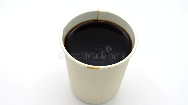 Drehen eines mit dunkelschwarzem Kaffee gefüllten normalen Papierbechers auf weißer Oberfläche stock video footage