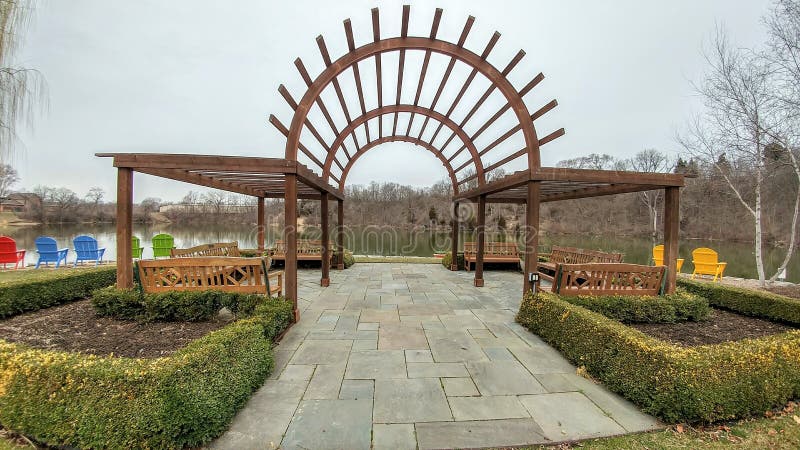 Rotary Gardens in Janesville, Wisconsin. Arched arbor overlooking lake and manicured evergreen trees. Colorful wooden chairs look out over lake. Rotary Gardens in Janesville, Wisconsin. Arched arbor overlooking lake and manicured evergreen trees. Colorful wooden chairs look out over lake.