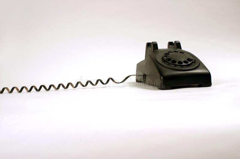 An old black rotary phone on a white background with the cord stretched taut, receiver out of picture. An old black rotary phone on a white background with the cord stretched taut, receiver out of picture