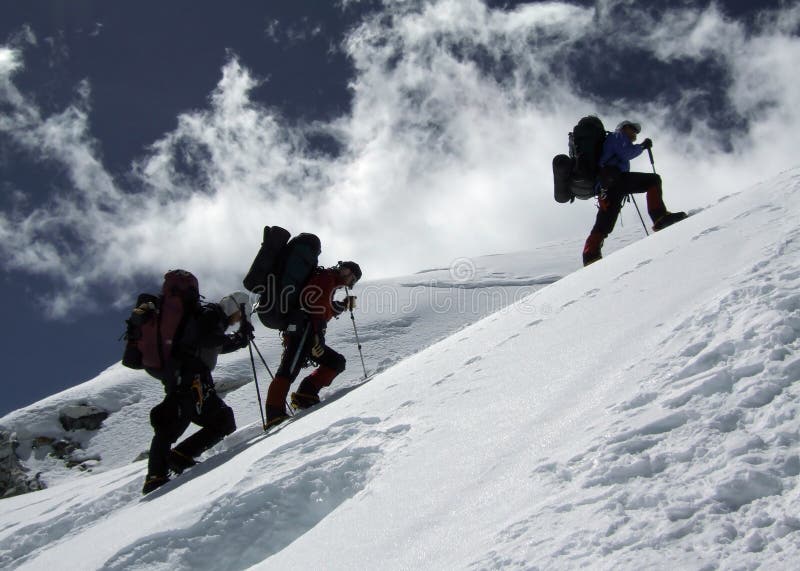 Three mountaineers with backpacks climbing a snowy ridge. Three mountaineers with backpacks climbing a snowy ridge