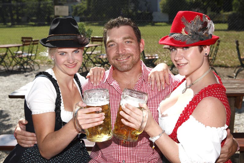 Drei Bayern in den traditionellen Kostümen, die in einem Bier sitzen, arbeiten im Garten stockbild Drei Bayern in den traditionellen Kostümen, die in einem Bier sitzen, arbeiten im Garten stockbild