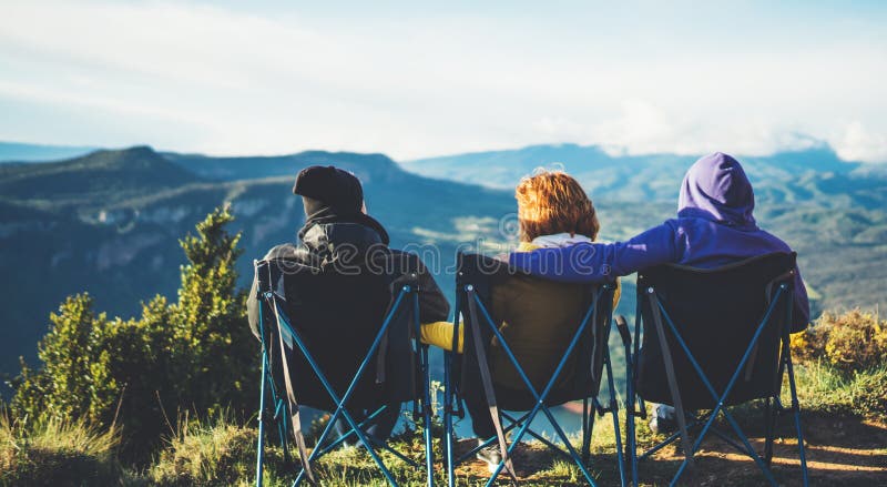 Drei Freunde sitzen in kampierenden Stühlen auf einen Berg, genießen Reisende Natur und Umarmung, Touristen untersuchen Abstand a