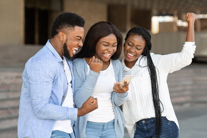 Drei glückliche afrikanische Freunde feiern Erfolg mit Smartphone im Freien lizenzfreie stockbilder Drei glückliche afrikanische Freunde feiern Erfolg mit Smartphone im Freien lizenzfreie stockbilder