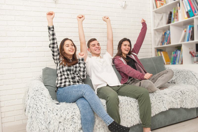 Drei Jugendfans sitzen im der Couch und dem aufpassenden Fernsehen lizenzfreies stockfoto Drei Jugendfans sitzen im der Couch und dem aufpassenden Fernsehen lizenzfreies stockfoto