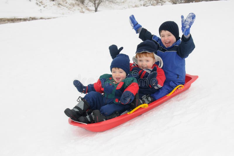 Three preschool-aged boys have fun together sliding downhill on a pleasant winter day. Three preschool-aged boys have fun together sliding downhill on a pleasant winter day.