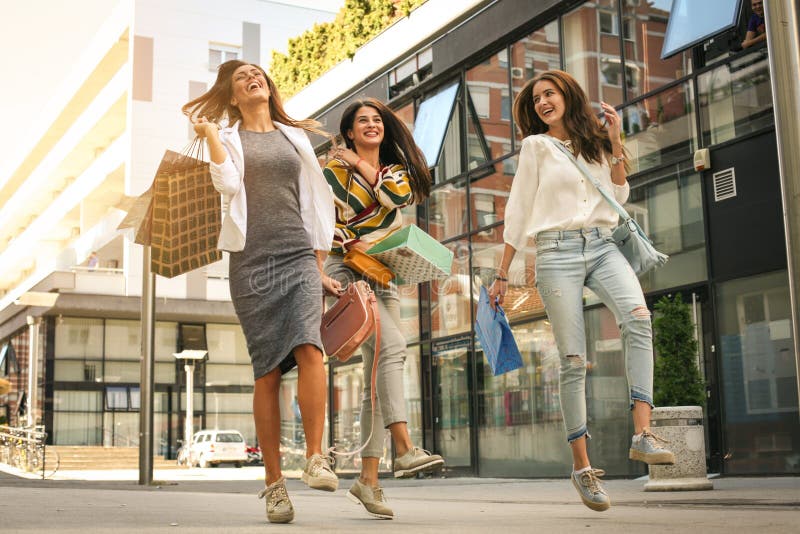 Drei moderne junge Frauen, die mit Einkaufstaschen schlendern Sati