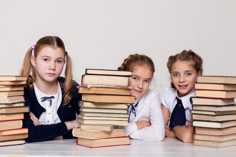 Drei Mädchen mit Schulbüchern für das Studium sitzen am Schreibtisch im Klassenzimmer lizenzfreie stockfotografie
