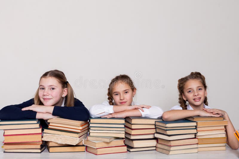 Drei Mädchenschulmädchen an einem Schreibtisch mit Büchern auf der Lektion in der Schule stockfotos