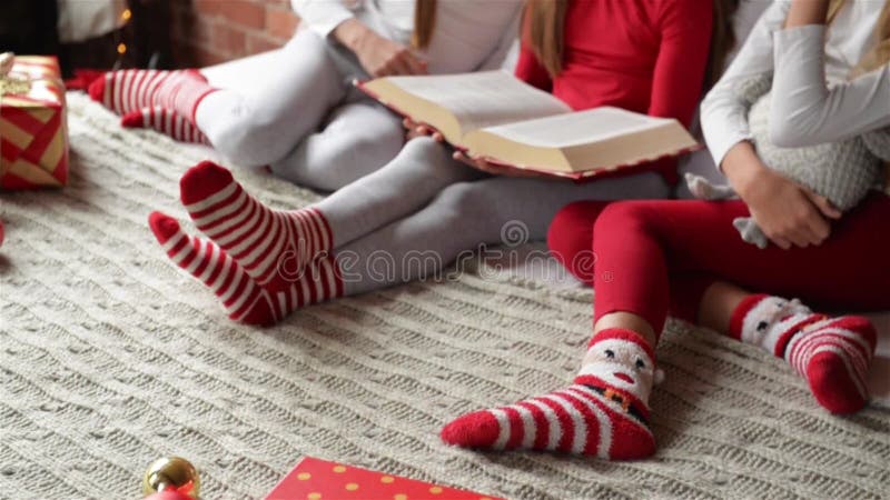 Drei Schwestern, die auf dem Bett in den weichen Pyjamas sitzen, Dreiergruppen, die Mädchen ein Buch von Weihnachtsgeschichten, S