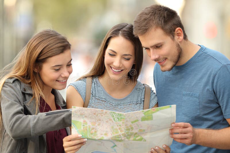 Drei Touristen, die eine Papierkarte auf der Straße konsultieren stockbilder Drei Touristen, die eine Papierkarte auf der Straße konsultieren stockbilder
