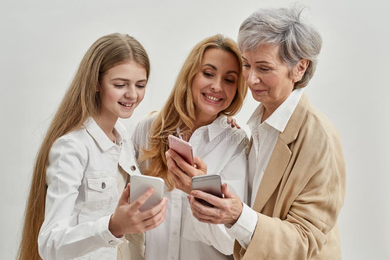 Drei Weibchen lächeln, wie sie Smartphones benutzen und gucken stockbilder