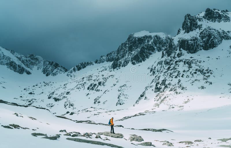 Dressed bright orange jacket backpacker man with trekking poles and backpack trekking by the mountain valley during high altutude