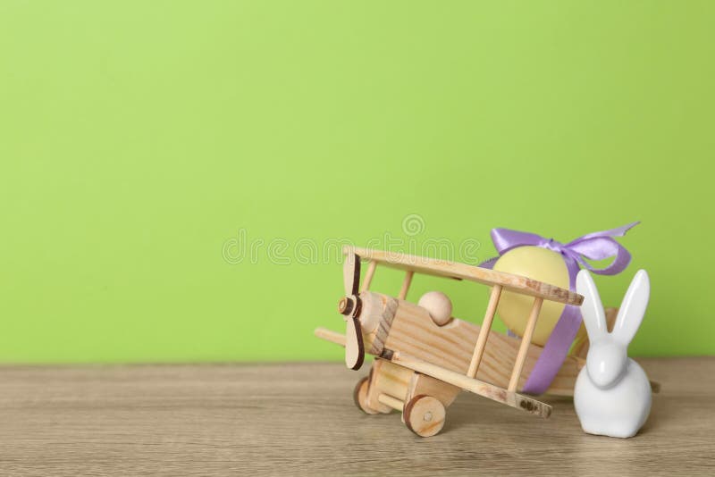 Wooden airplane with dyed egg and cute Easter bunny on table against color background, space for text. Wooden airplane with dyed egg and cute Easter bunny on table against color background, space for text