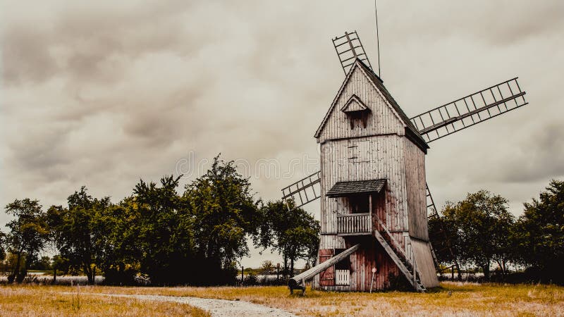 Drewniany wiatrak w wiejskim krajobrazie letnim pod chmurami burzy. Letni krajobraz z widokiem na centrum drewnianego, historycznego wiatraka, który był młynem z chmurami burzowymi