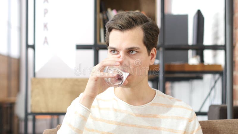 Dricksvattensammanträde för ung man på en soffa som är hemmastadd och ser kameran royaltyfri bild Dricksvattensammanträde för ung man på en soffa som är hemmastadd och ser kameran royaltyfri bild