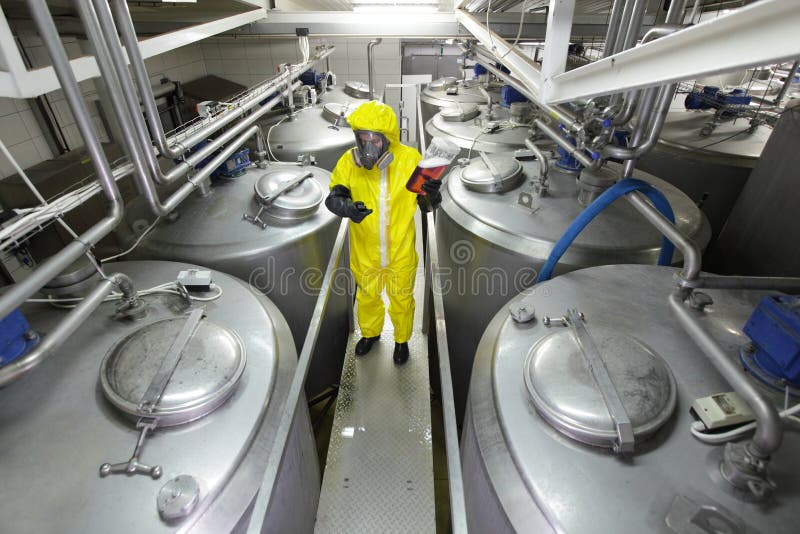 Drie arbeiders die bij grote zilveren tanks in installatie werken stock afbeelding Drie arbeiders die bij grote zilveren tanks in installatie werken stock afbeelding