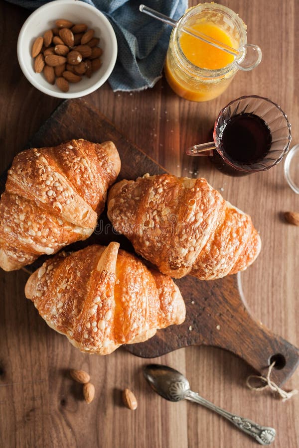 Drie croissants met kaaskorst liggen op een houten raad op een houten lijst naast thee, amandelen, abrikozenjam en lepel royalty-vrije stock afbeeldingen Drie croissants met kaaskorst liggen op een houten raad op een houten lijst naast thee, amandelen, abrikozenjam en lepel royalty-vrije stock afbeeldingen