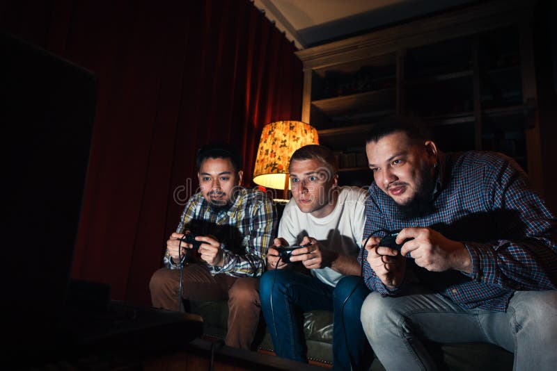 Drie geconcentreerd jong het huisvideospelletje van het kerelspel royalty-vrije stock foto Drie geconcentreerd jong het huisvideospelletje van het kerelspel royalty-vrije stock foto