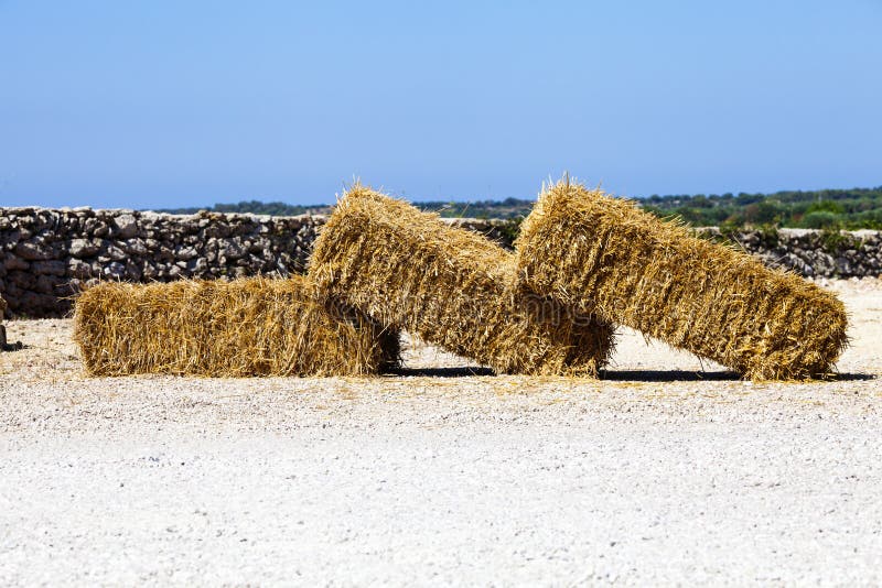 Three hay bales resting on the ground. As a domino effect. Outdoor behind a long wall and blue sky. Italian scene in Apulia (Italian region), Italy. Three hay bales resting on the ground. As a domino effect. Outdoor behind a long wall and blue sky. Italian scene in Apulia (Italian region), Italy.