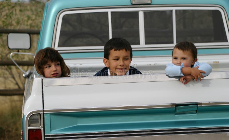 Three Hispanic American children, each with different expressions, hanging out in the back of an old pick up truck. Three Hispanic American children, each with different expressions, hanging out in the back of an old pick up truck.
