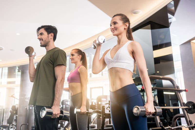 Drie jongeren die terwijl de afwisselende domoor bicep krult glimlachen stock fotografie Drie jongeren die terwijl de afwisselende domoor bicep krult glimlachen stock fotografie