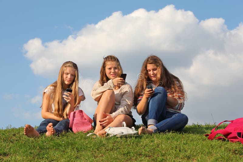 Drie meisjes zitten op gras met mobiele telefoons royalty-vrije stock afbeelding Drie meisjes zitten op gras met mobiele telefoons royalty-vrije stock afbeelding