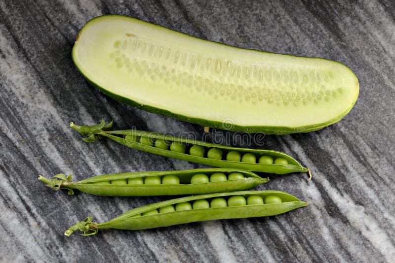Drie peulen van groene erwten en komkommer op een granietplaat stock fotografie Drie peulen van groene erwten en komkommer op een granietplaat stock fotografie